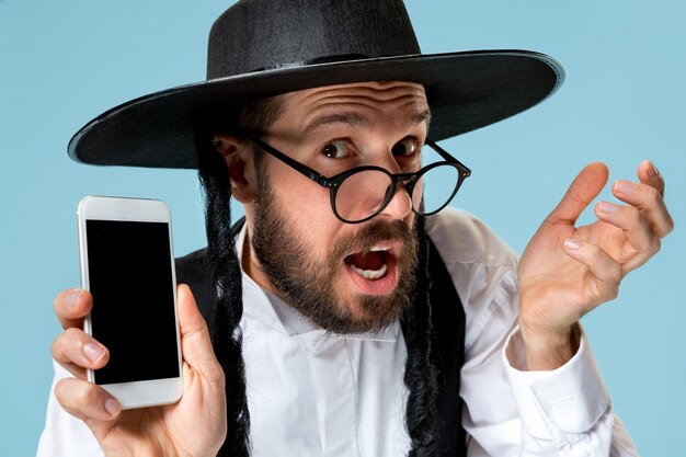 Retrato de un joven judío ortodoxo con teléfono móvil en el estudio. Purim, negocios, empresario, festival, fiesta, celebración, judaísmo, concepto de religión.