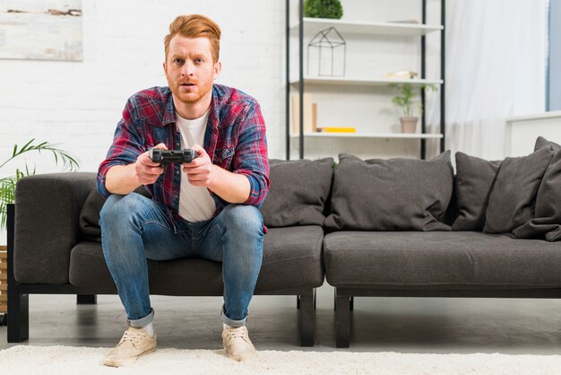 Retrato de un joven jugando al videojuego con un joystick sentado en la sala de estar