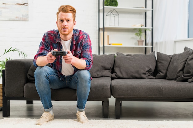 Retrato de un joven jugando al videojuego con un joystick sentado en la sala de estar