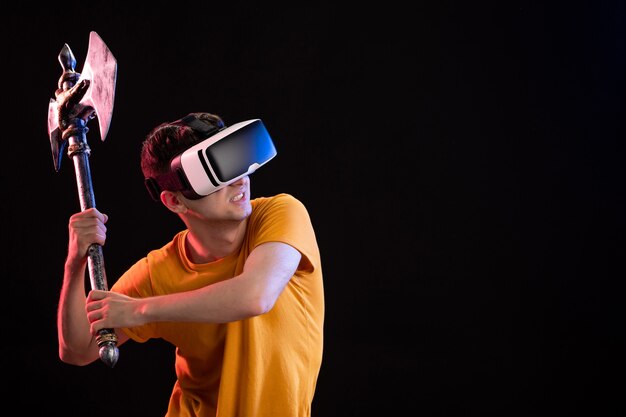 Retrato de joven jugando vr con hacha de batalla en la pared oscura