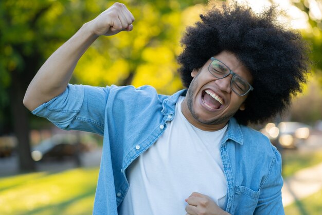 Retrato de joven latino celebrando la victoria al aire libre. Concepto urbano. Concepto de éxito.