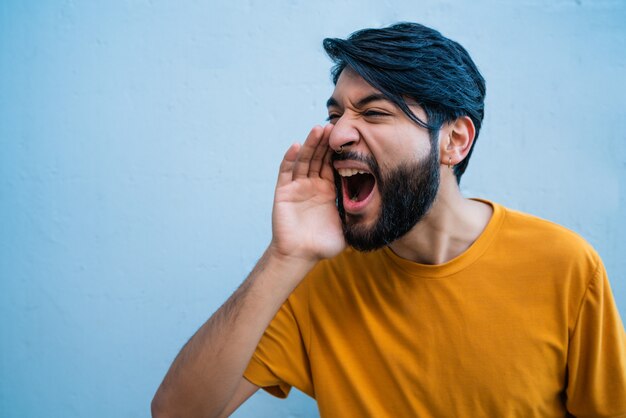 Retrato de joven latino gritando y gritando contra el fondo azul.