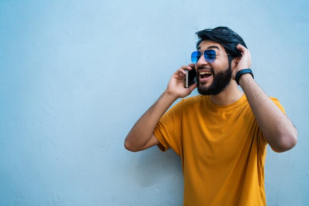 Retrato de joven latino hablando por teléfono contra azul. Concepto de comunicación.