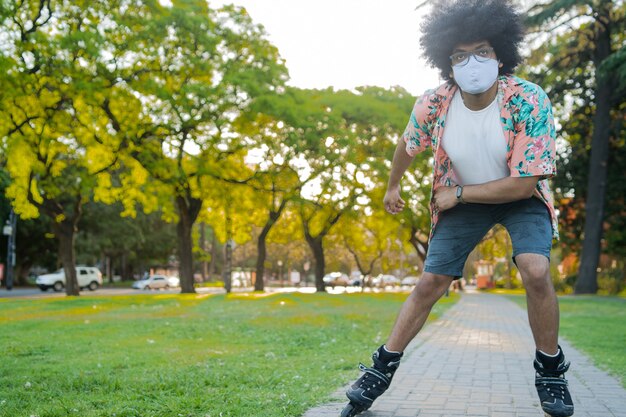 Retrato de joven latino con mascarilla mientras patina al aire libre en la calle