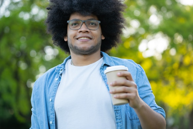 Retrato de joven latino sosteniendo una taza de café mientras camina al aire libre en la calle