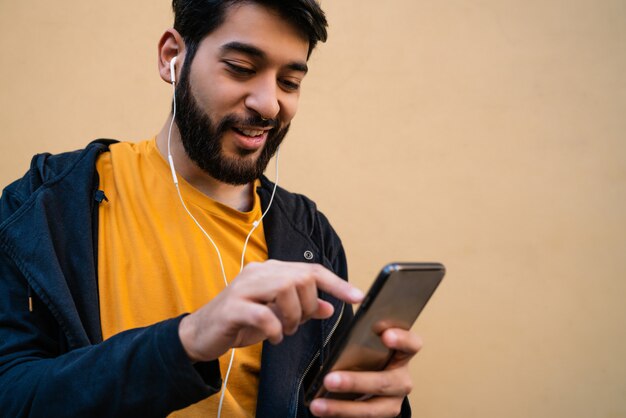 Retrato de joven latino usando su teléfono móvil con auriculares contra amarillo