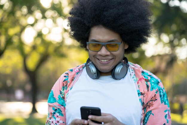 Retrato de joven latino usando su teléfono móvil mientras está de pie al aire libre en la calle. Concepto urbano