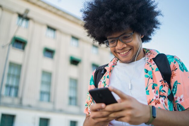 Retrato de joven latino usando su teléfono móvil mientras está de pie al aire libre en la calle