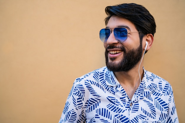 Retrato de joven latino vistiendo ropa de verano y escuchando música con auriculares contra amarillo.