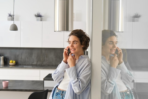 Retrato de una joven linda que responde una llamada telefónica, habla en su teléfono inteligente, pasa tiempo en casa.