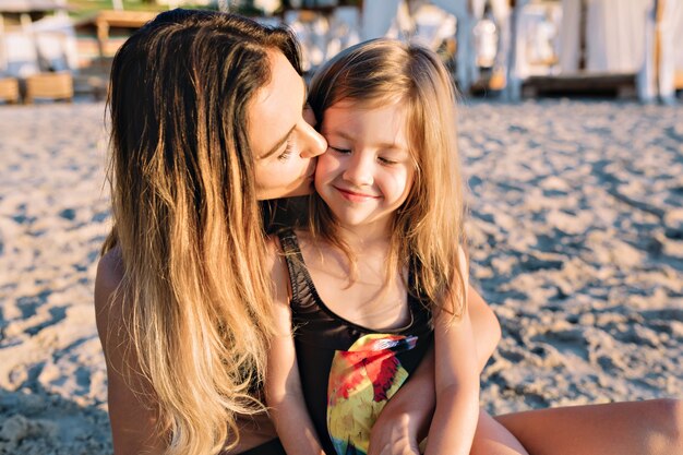 Retrato de joven madre atractiva con hermosa hija vestida con trajes de baño negros en la playa de verano de cerca