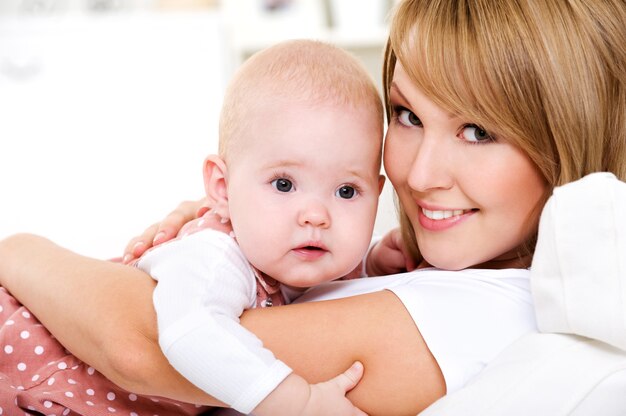 Retrato de joven madre feliz con bebé recién nacido en casa