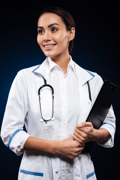 Retrato de joven médico alegre sosteniendo portapapeles y mirando a un lado