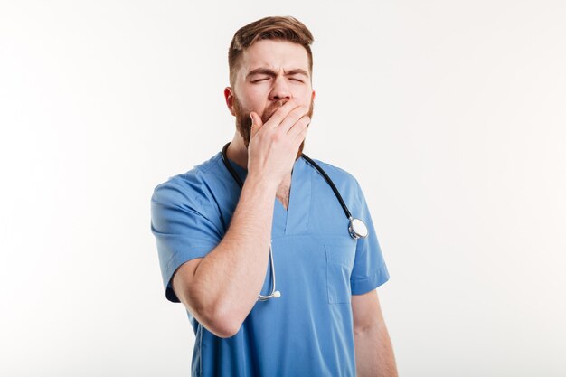 Retrato de un joven médico cansado bostezo aislado