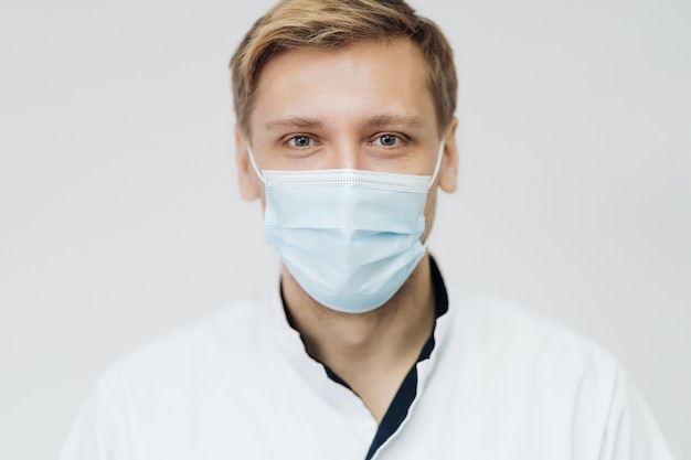 Retrato de un joven médico masculino usar máscara estéril aislada en la pared blanca