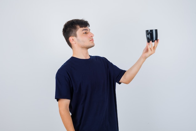 Retrato de joven mirando una taza de té en camiseta negra y mirando pensativo vista frontal