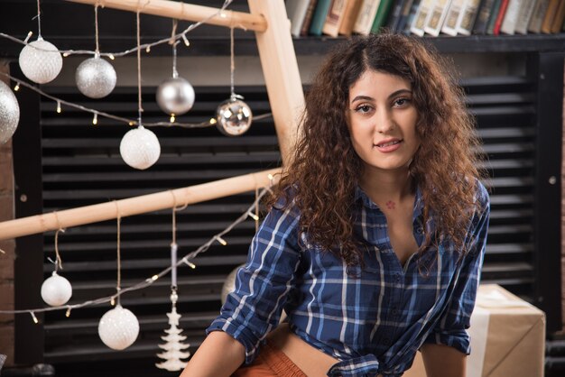 Retrato de una joven modelo en camisa a cuadros posando cerca de bolas de Navidad