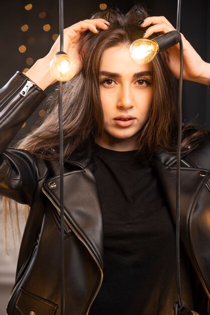 Retrato de una joven modelo en chaqueta de cuero negro posando junto a las lámparas.