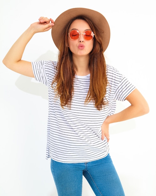 Retrato de joven modelo elegante mujer riendo en ropa casual de verano en sombrero marrón con maquillaje natural aislado en la pared blanca. Dando beso de aire