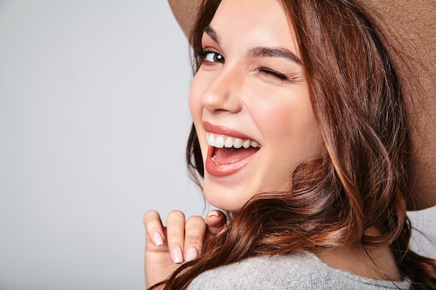 Retrato de joven modelo elegante riendo en ropa casual gris de verano en sombrero marrón con maquillaje natural