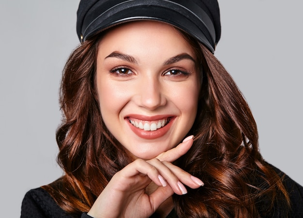 Retrato de joven modelo elegante riendo en ropa casual de verano negro en gorra con maquillaje natural en gris