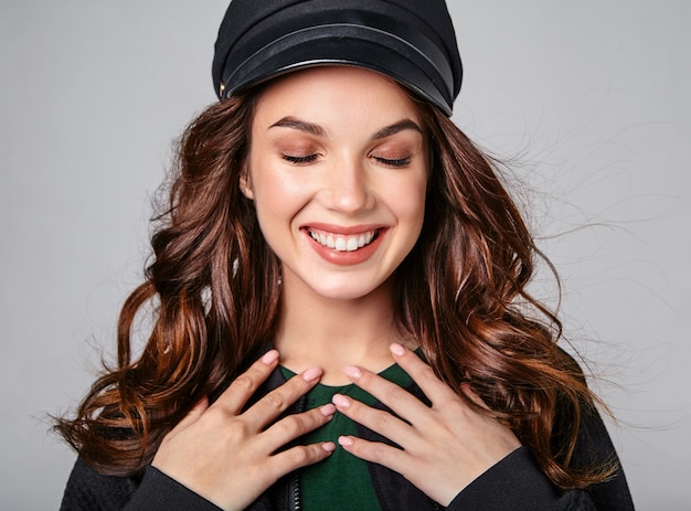 Retrato de joven modelo elegante riendo en ropa casual de verano negro en gorra con maquillaje natural en gris