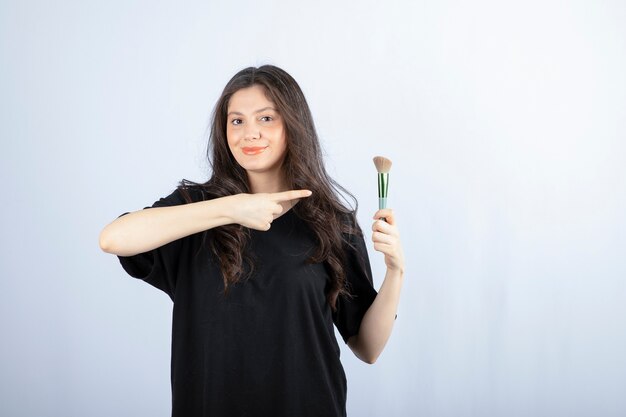 Retrato de joven modelo con maquillaje con pincel de pie en blanco.