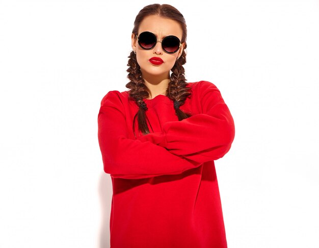 Retrato de joven modelo de mujer sonriente feliz con maquillaje brillante y labios coloridos con dos coletas y gafas de sol en ropa de verano rojo aislado. Brazos cruzados