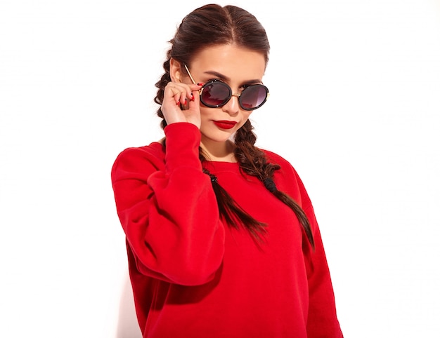 Retrato de joven modelo de mujer sonriente feliz con maquillaje brillante y labios coloridos con dos coletas y gafas de sol en ropa de verano rojo aislado. Detrás de las gafas de sol de moda