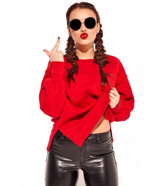 Retrato de joven modelo de mujer sonriente feliz con maquillaje brillante y labios coloridos con dos coletas y gafas de sol en ropa de verano rojo aislado. mostrando signo de mierda