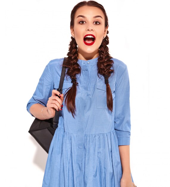 Retrato de joven modelo de mujer sonriente feliz con maquillaje brillante y labios rojos con dos coletas en manos en verano colorido vestido azul y mochila aislado