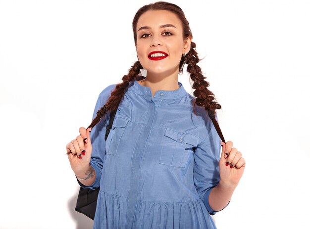 Retrato de joven modelo de mujer sonriente feliz con maquillaje brillante y labios rojos con dos coletas en manos en verano colorido vestido azul y mochila aislado