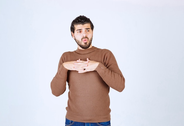 Retrato de un joven modelo de pie y cogidos de la mano en el pecho.