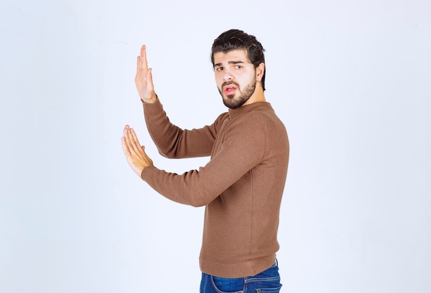 Retrato de un joven modelo de pie y empujando un objeto imaginario. Foto de alta calidad