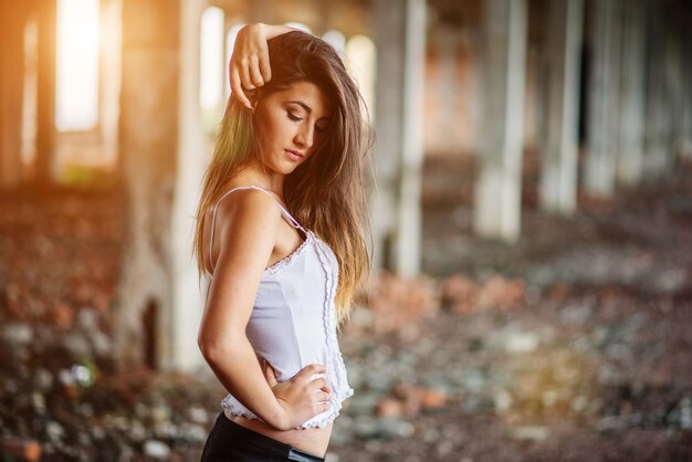 Retrato de una joven morena linda con pantalones de cuero negro y blusa blanca posada en un lugar abandonado