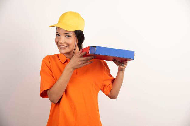 Retrato de joven morena con pizza en caja en pared blanca.