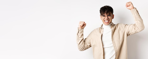 Retrato de un joven motivado que siente alegría levantando las manos y celebrando la victoria triunfando y