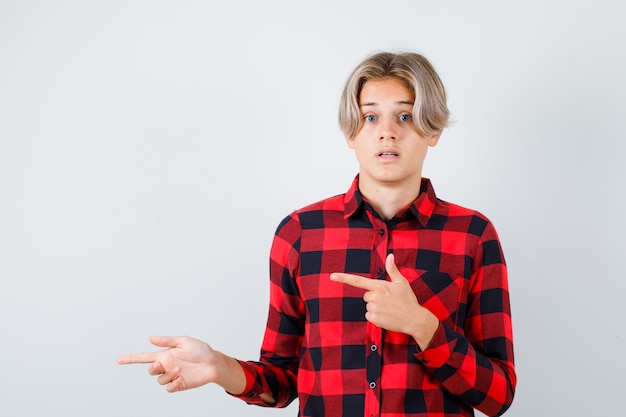 Retrato de joven muchacho adolescente apuntando hacia la izquierda en camisa a cuadros y mirando ansiosa vista frontal