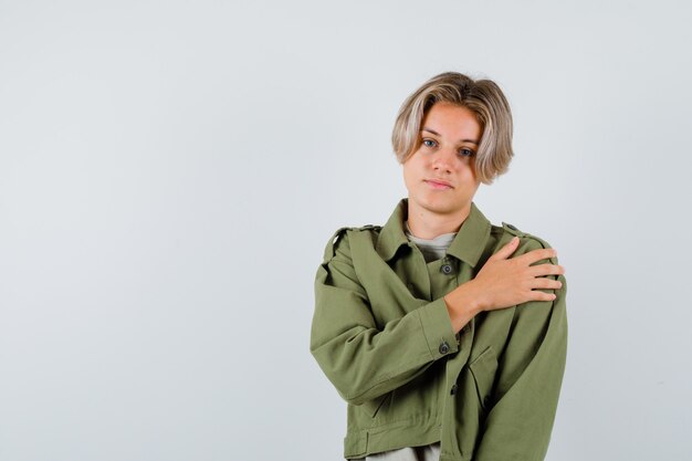 Retrato de joven muchacho adolescente con la mano en el hombro en chaqueta verde y mirando confiado vista frontal