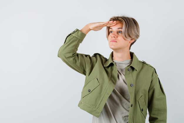 Retrato de joven muchacho adolescente mirando lejos con las manos sobre la cabeza en chaqueta verde y mirando enfocado vista frontal