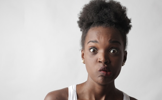 Retrato de una joven mujer afroamericana haciendo una cara divertida de pie contra una pared blanca