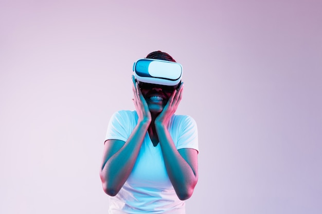 Retrato de joven mujer afroamericana jugando en gafas VR en luz de neón en gradiente