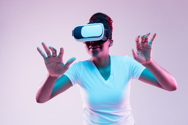 Retrato de joven mujer afroamericana jugando en gafas VR en luz de neón en gradiente