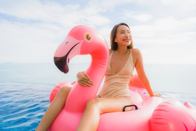 Retrato joven mujer asiática en flotador inflable flamingo alrededor de la piscina al aire libre en el hotel resort