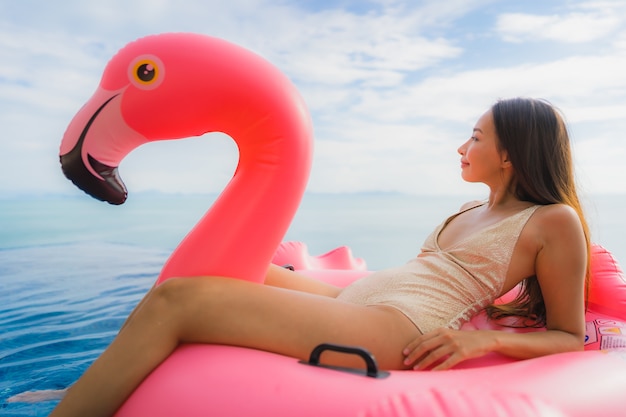 Retrato joven mujer asiática en flotador inflable flamingo alrededor de la piscina al aire libre en el hotel resort