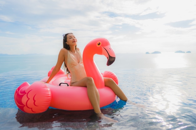 Retrato joven mujer asiática en flotador inflable flamingo alrededor de la piscina al aire libre en el hotel resort