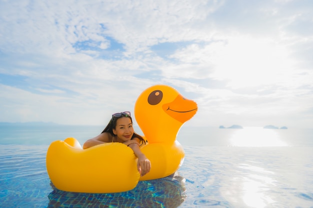 Retrato joven mujer asiática en flotador inflable pato amarillo alrededor de la piscina al aire libre en el hotel y resort