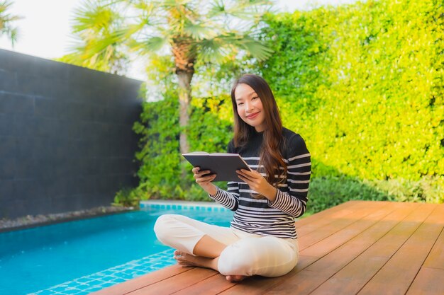 Retrato joven mujer asiática leer libro alrededor de la piscina al aire libre