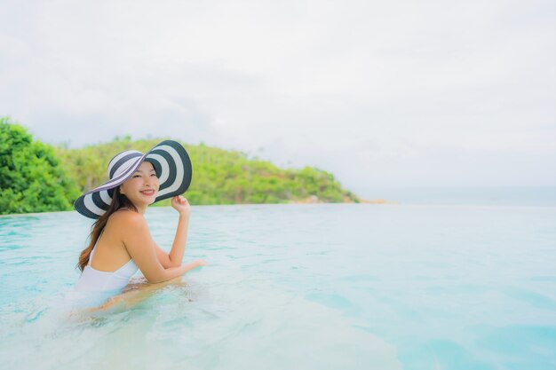 Retrato joven mujer asiática relajarse sonrisa feliz alrededor de la piscina al aire libre en el hotel resort con vista al mar