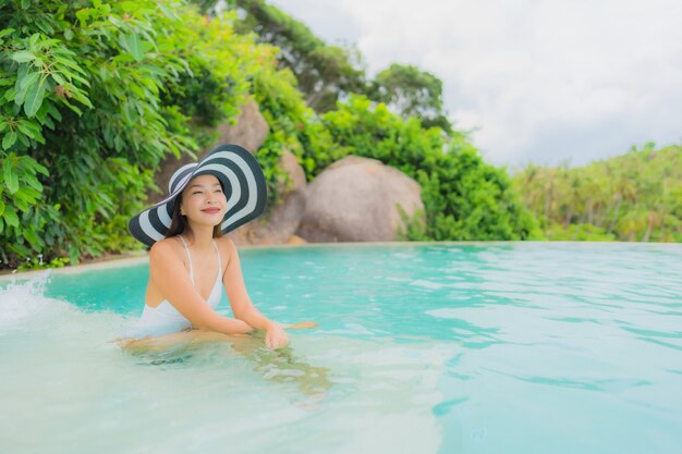 Retrato joven mujer asiática relajarse sonrisa feliz alrededor de la piscina al aire libre en el hotel resort con vista al mar